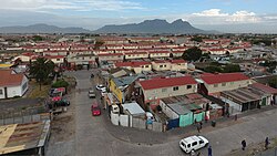 A view of Manenberg looking towards Table Mountain in the background. The red roofed government housing blocks in which a large proportion of the community's population lives can be seen in the foreground.