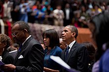 Obama en zijn vrouw staan ​​in een volle kerk, kijken vooruit, met hun mond open midden in een zin terwijl ze een gebed opzeggen.
