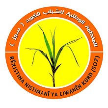 Round logo of a grass plant against a yellow background, with the organization's name in Kurdish and Arabic on an orange border