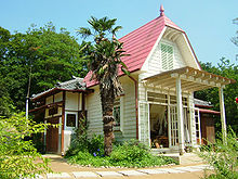 Casa branca com telhado vermelho rodeada de vegetação.