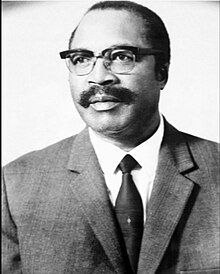 A black-and-white photo of a man wearing a suit and glasses.