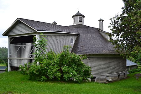 Grange circulaire Damase-Amédée-Dufresne près de Saint-Benoit-du-Lac en Estrie au Québec en juillet 2017. Sous les arbres, elle est nichée derrière une maison bourgeoise près du lac Memphrémagog.