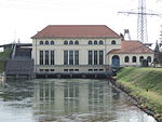 A white power plant with numerous windows with water flowing below the building