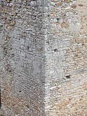 Photographie en couleurs de blocs de pierre de forme régulière au milieu de la maçonnerie plus irrégulière d'un mur.