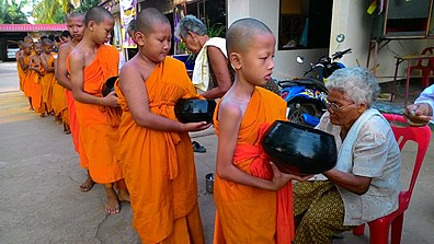Noviisimunkkeja eli oppipoikia keräämässä almuja. Ihmiset antavat ruokaa munkkien astioihin. Buddhalaisuudessa anteliaisuus ja hyväntekeväisyys ovat tärkeitä hyveitä, jotka auttavat tiellä kohti valaistumista.