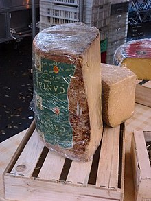 Gros cylindre de fromage d’une trentaine de centimètre presque aussi large que haut, coupé dans le sens de la hauteur. Il est présenté sur des cageots en bois.