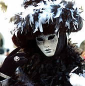 Eine Person beim Karneval in Venedig in einer traditionellen venezianischer Verkleidung für Frauen mit Gesichtsmaske und einer farblichen Komposition in Silber und Schwarz