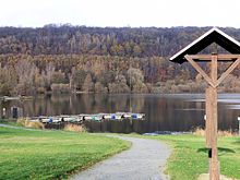 Blick aus Richtung Vienenburg auf den See, eine Informationstafel, die Steganlage und den Harlyberg