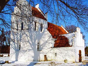 Photographie d'une église romane peinte en blanc et couverte de tuiles sous la neige.