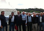 En mand i jakkesæt er omgivet af andre mænd i et rugbystadion nær en reception.