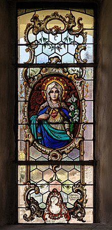 Un vitrail sur fond tamisé avec en médaillon une vierge marie multicolore mettant son coeur bien en évidence.