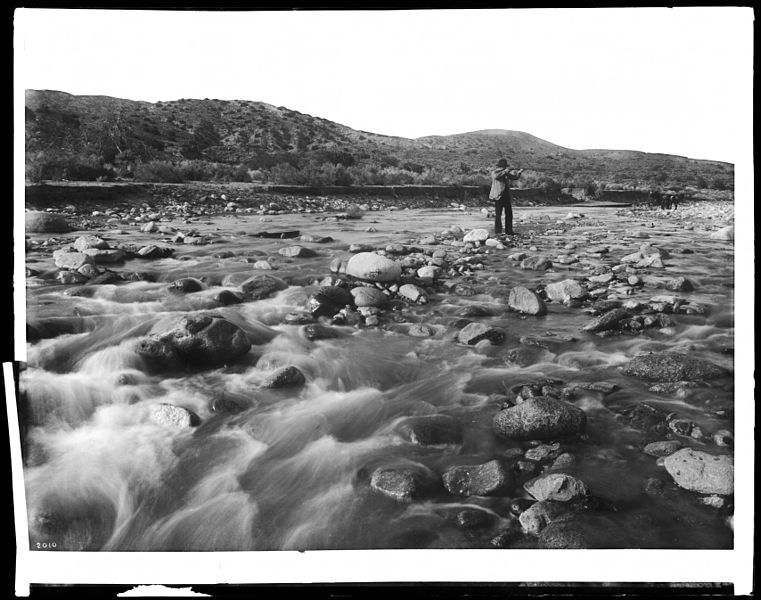 File:Man with rifle stands in mountain stream as it floods, east of Palmdale, California, ca.1920 (CHS-2010).jpg