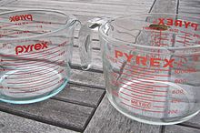 Two clear measuring jugs featuring red text. The jug on the right is wider than the jug on the left.