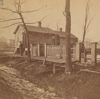 The cottage of Catherine and Patrick O'Leary, 137 (now 558) W. DeKoven St. As this view suggests, the neighborhood was congested with mean wooden buildings and a variety of industry, a condition which helped to spread the fire of 1871 as rapidly as it did. A strong wind blowing towards the northeast spared the O'Leary cottage and the buildings seen here to its west. From a stereoptican view by A.H. Abbott, Photographer, whose studio at 976 (now 2201) N. Clark Street was consumed by the flames. 137 DeKoven Street 1871.png