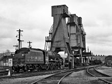 Preserved LMS Jubilee Class No.5690 Leander moves towards the ash tower with the giant cast-concrete coal stage beyond at Carnforth MPD, built during the 1944 reconstruction of the shed 5690 LEANDER at Carnforth.jpg