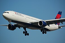 A large twin-engined jet aircraft with its landing gear down. The plane is painted white, with a navy and blue vertical stablizer, and blue jet engine housings.