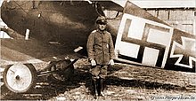 Photo en noir et blanc d'un homme en uniforme, debout devant un avion sur lequel on voit une grande svastika noire sur fond blanc.