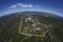 Plusieurs constructions dispersées au milieu d'un site cerné d'une roue avec en arrière plan des collines