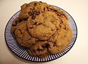 A plate of chocolate chip cookies on a blue and white striped plate. The plate sits on a beige surface.
