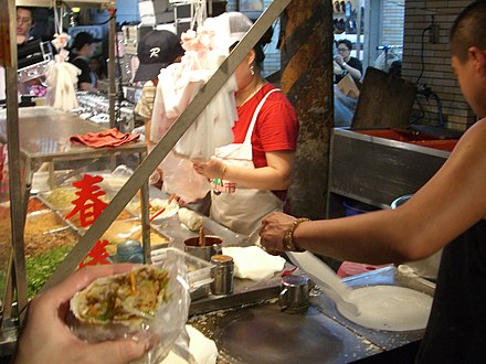 A popiah vendor in Keelung, Taiwan. Popiah crepes are produced through "rubbing" (foreground) and then filled and rolled (background)