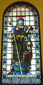 St James is shown in layered robes holding a staff across his body and a Bible in his left hand. On his right shoulder is the scallop shell.