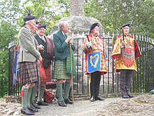 The Honourable Adam Bruce (far right) at his installation as Finlaggan Pursuivant of Arms of Clan Donald. Finlaggan wears a tabard emblazoned with the arms of his employer, the Chief of Clan Donald. Adam Bruce Finlaggan and Charles Burnett Ross.jpg