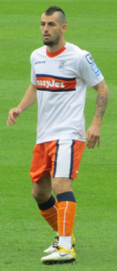 Bir maç sırasında beyaz ve turuncu renklerde bir futbolcu.