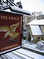 The main signboard of The Eagle pub in the snow on Bene't Street, as seen from the Corpus Christi College accommodation above