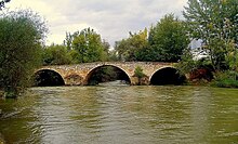 a three arch bridge over a river with lots of water and trees along the banks