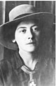 Porträt einer schlanken Frau mit zusammengebundenen Haaren und dunklen Augen, die eine dunkle Bluse und einen Hut trägt