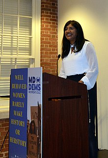 Aruna Miller standing at a podium with a sign for the Maryland Democratic Party on its front side