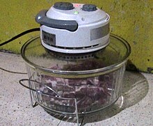 A tabletop convection oven cooking pork. For slower cooking, the gridiron here has been reversed to place the meat low and far from the main heat source (at the top of the pot), although near the heat of the glass pot's bottom. Flipping the gridiron would raise the meat closer to the main heat source. Tabletop convection oven.jpg