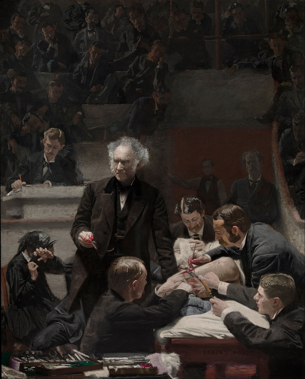 A wall of darkened spectators frame the background as the light illuminates a group of men cutting into a sedated figure (obscured by leaning figures and cloths) as part of a medical class circa 1875