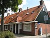 Blok met 8 woningen, gecombineerde toegangen van twee woningen onder een ingestoken schilddak, zijkant met houten topgevel, aan oostkant toegangspoort tot binnenterrein, onderdeel van complex bejaardenwoningen in Tuindorp Nieuwendam