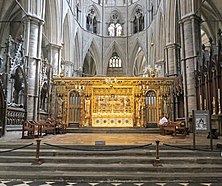 A golden altar and screen in the centre of a grey stone church.