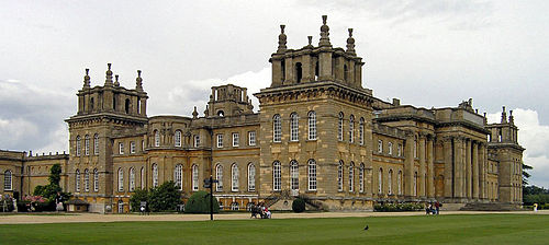 Exterior of a large English Baroque palace fronted by lawns