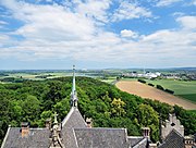 Blick nach Osten in das Leinetal von der Aussichtsplattform des Schlosses Marienburg auf dem Bergfried. Im Vordergrund blickt man auf den bewaldeten Marienberg mit dem Schulenburger Forst, davor auf die Dächer der Burgkapelle und der Marienburg.