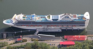 A cruise ship is viewed from above, where the ship's pools, funnels, and top decks are observed.