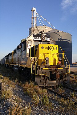 A yellow and black locomotive at rest by grain elevator