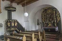 Barevná fotografie interiéru kostela se světlehnědými lavicemi, restaurovaným barokním oltářem a kazatelnou v tmavohnědých barvách