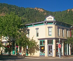 Dvoupatrová budova ze žlutých cihel na rohu ulic Hunter a Cooper s fialovým a zeleným lemováním. Špičatá část nad střechou je napsána velkými písmeny „1888“. V zadní části, v horní části obrázku, je zalesněný, skalní hřeben.
