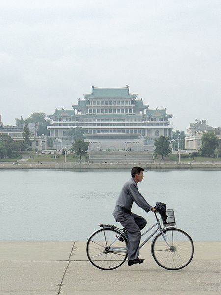 Seorang pria sipil berseragam mengendarai sepeda di Pyongyang. Seragam seperti ini adalah bagian dari peraturan busana yang diamanatkan negara secara nasional.