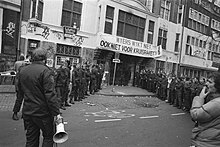 Black and white photograph of police and supporters of the squat facing off in front of the main entrance