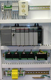 Control panel with PLC (gray elements in the center). The unit consists of separate elements, from left to right: power supply, controller, relay units for input and output. PLC Control Panel.png