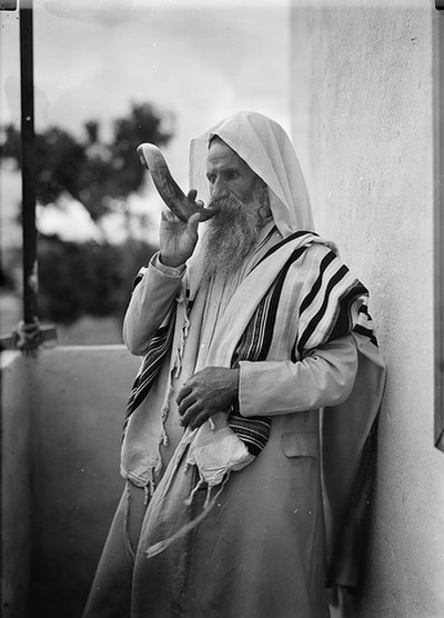 A man in a tallit blows the shofar