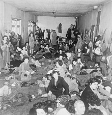 Schwarzweißfoto, das eine Gruppe von Frauen zeigt, die in eine Kaserne gedrängt werden