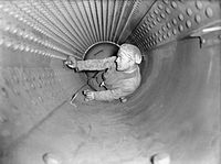 A stoker plugging a leaking boiler tube inside one of Curacoa's boilers at Rosyth, Scotland The Royal Navy during the Second World War A7256.jpg