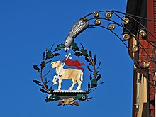 A pub cantilever attached to the building with a golden lamb framed by a wreath of oak leaves