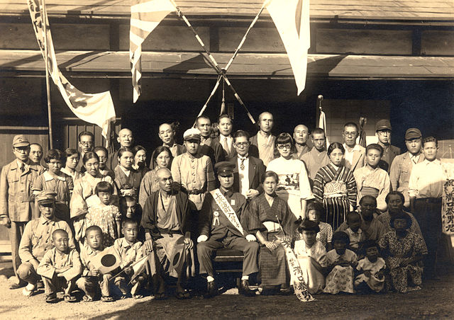 1930s photo of a military enrollment. The Hinomaru is displayed on the house and held by several children.