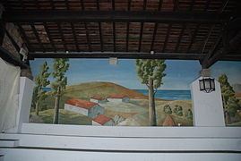 Photographie d’une fresque montrant un paysage de collines, avec des maisons, face à la mer.